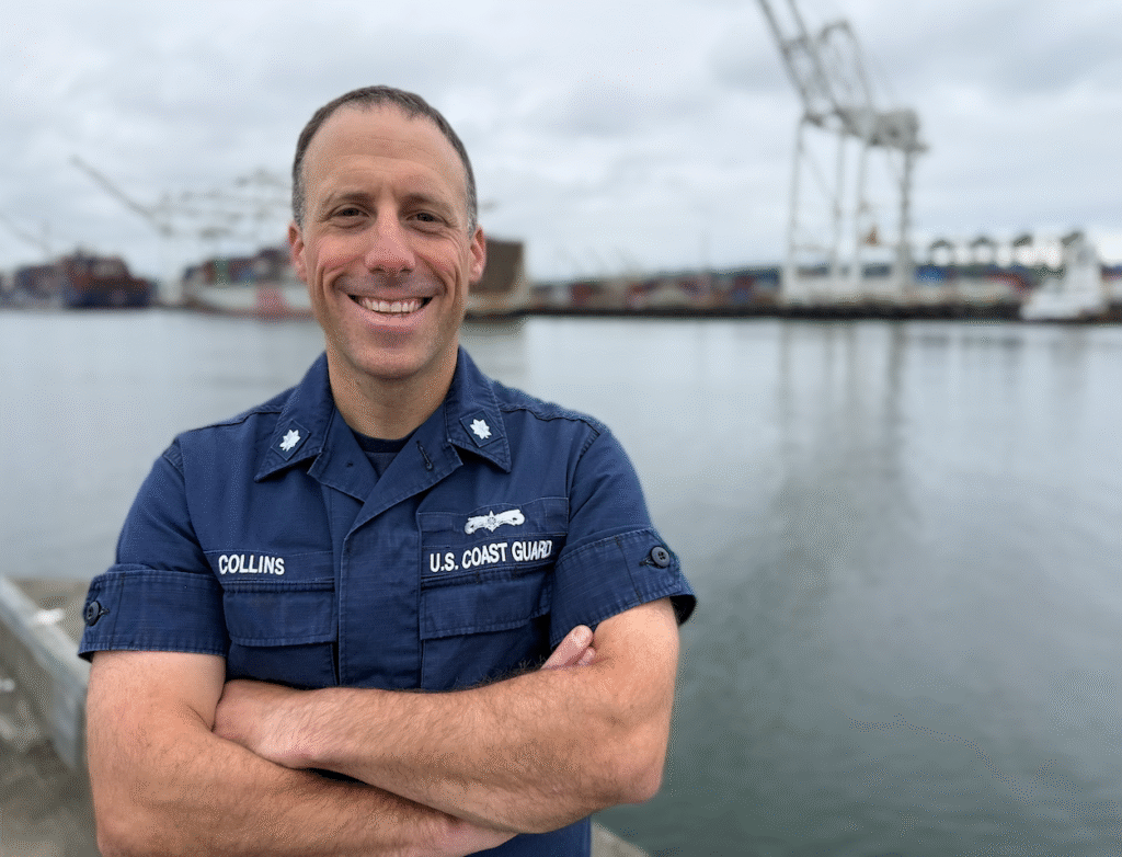 Landscape-orientation photograph of Jamie Collins standing in front of a port facility with container crane and a containership in the background.